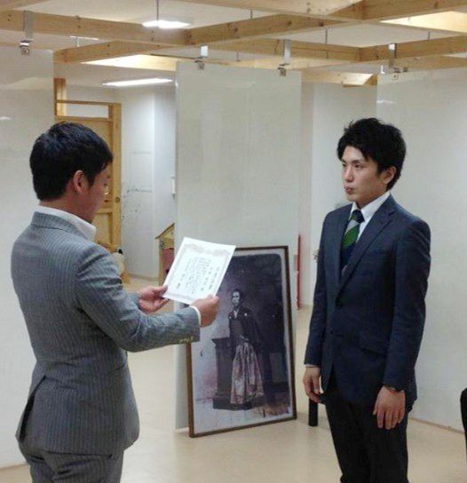 スーツ姿で式典に臨む松本じゅんや(右)